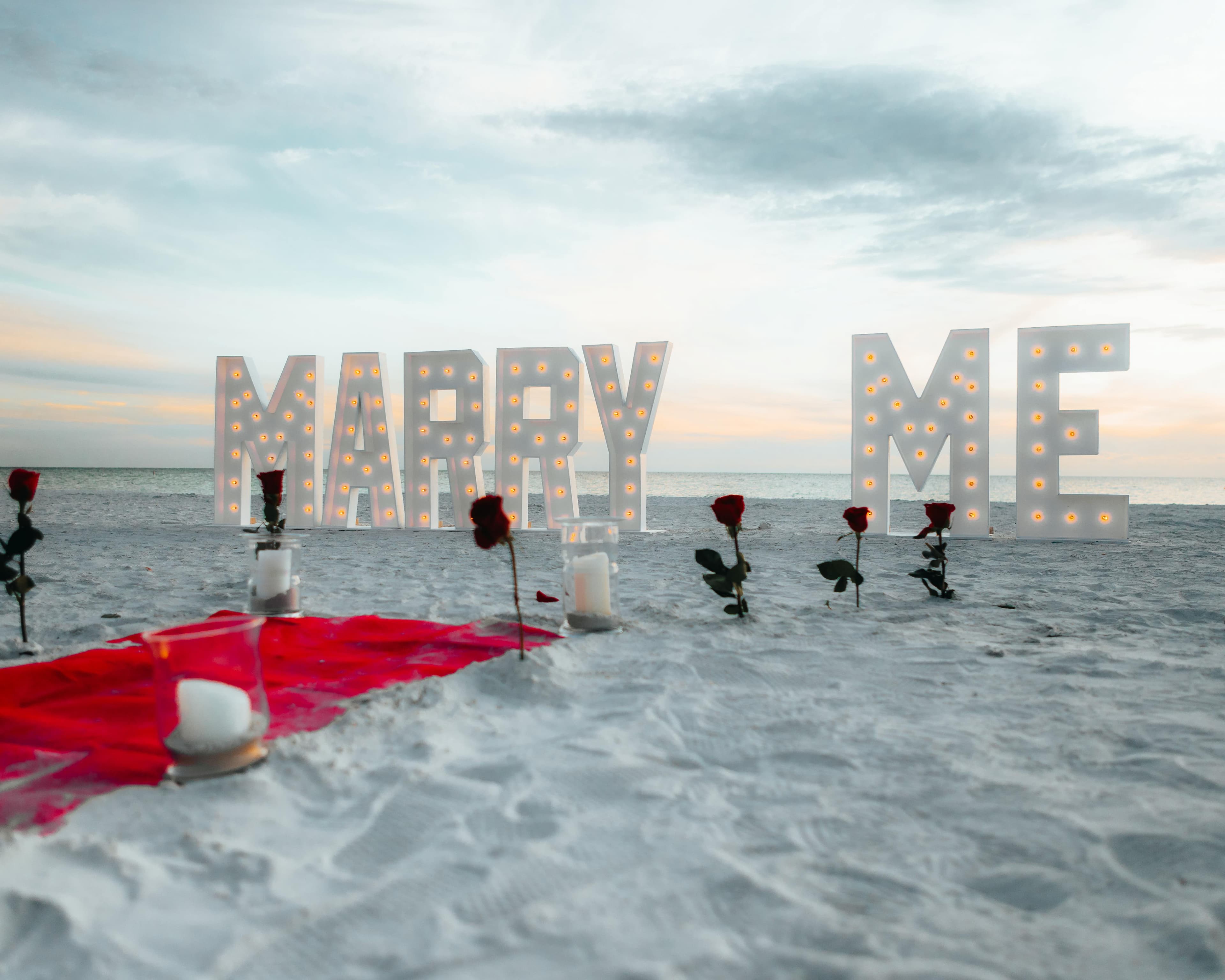 Romantic beach proposal setup with illuminated letters and roses